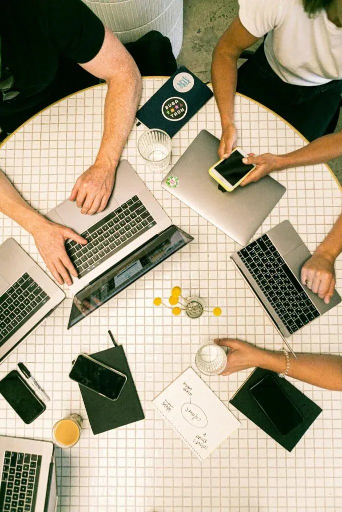 Group of individuals collaborating at a table with laptops and smartphones, emphasizing teamwork and digital marketing strategies for local SEO optimization.