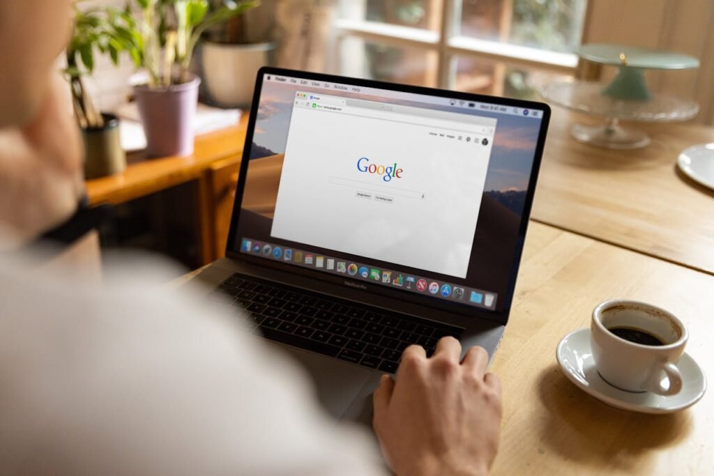 Person using a laptop to access Google search, with a coffee cup on a wooden table, emphasizing modern digital engagement and online presence for businesses.