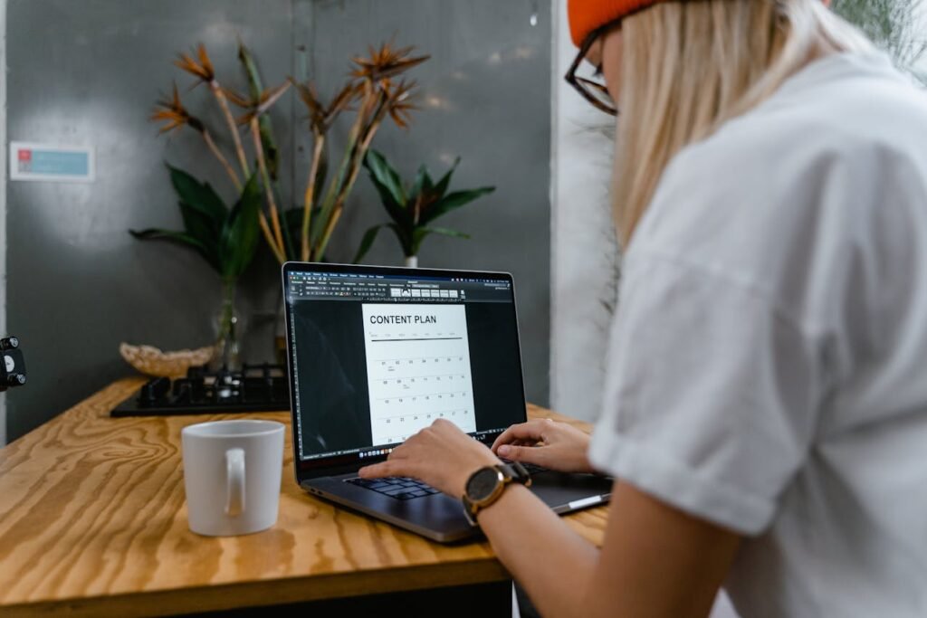 Person working on a laptop displaying a content plan, with a coffee mug and indoor plants in a modern workspace, emphasizing strategic content creation and brand communication.